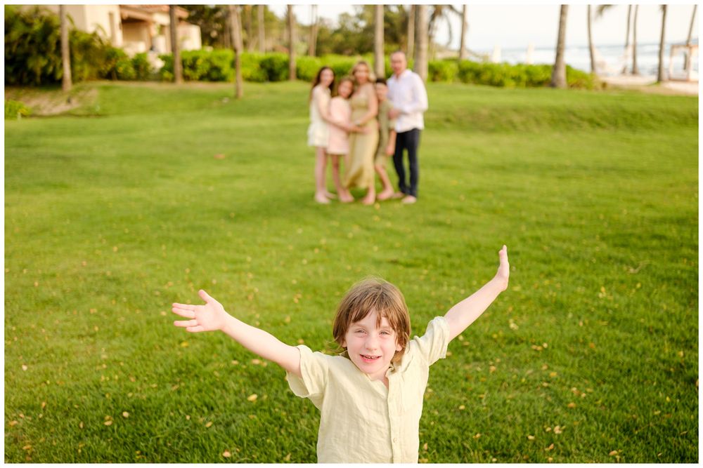 Child posing joyfully on a lawn with family in the background during a session at St. Regis Punta Mita.