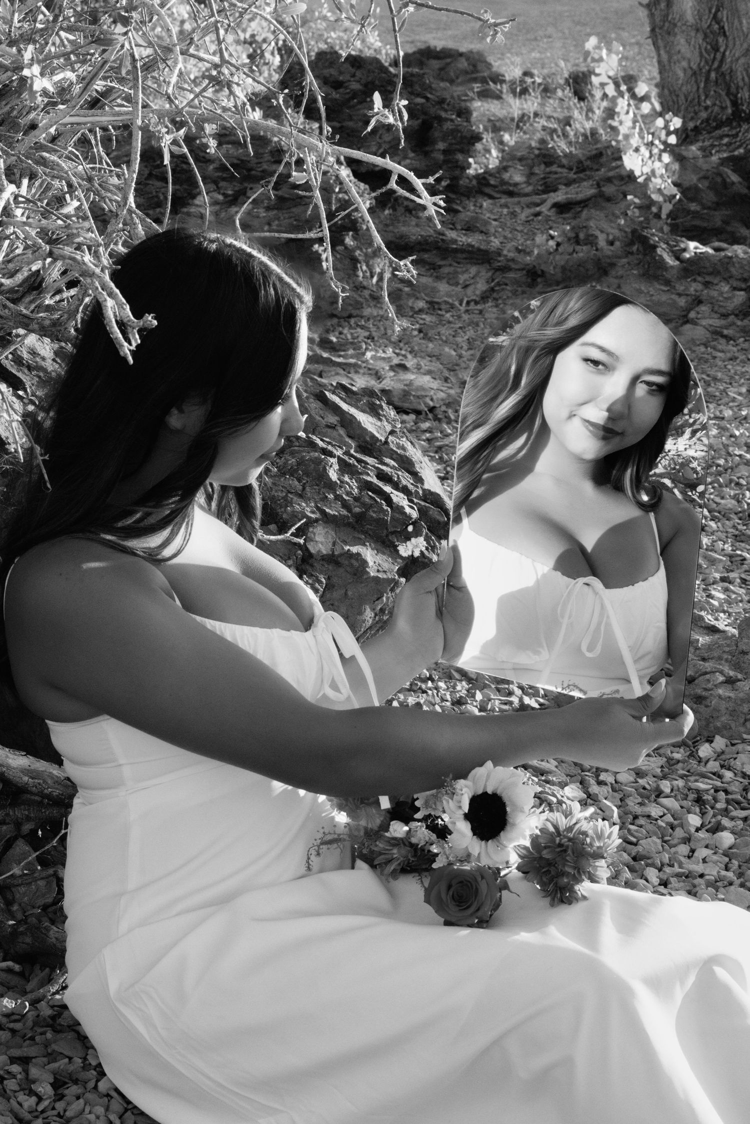 A series of black and white photos showing someone in a white dress lying in nature among flowers and foliage.