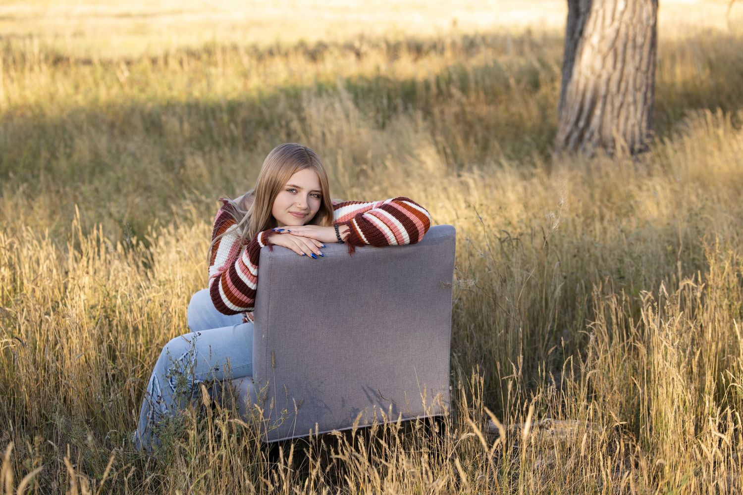 A person in jeans lies in golden grass at sunset holding a blank sign during a photo session.