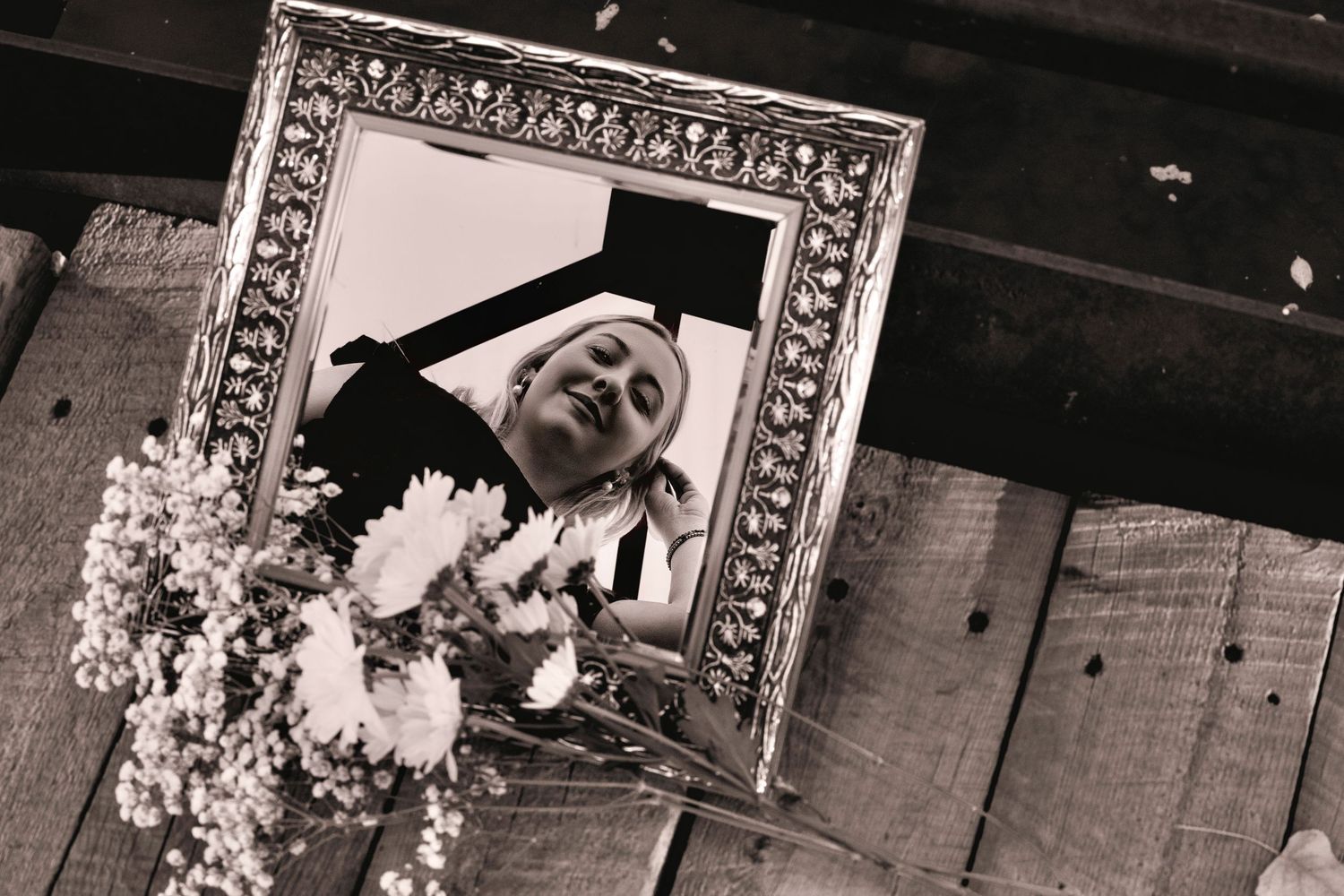 A black and white photograph shows a person walking past a wall decorated with framed artwork and floral arrangements.