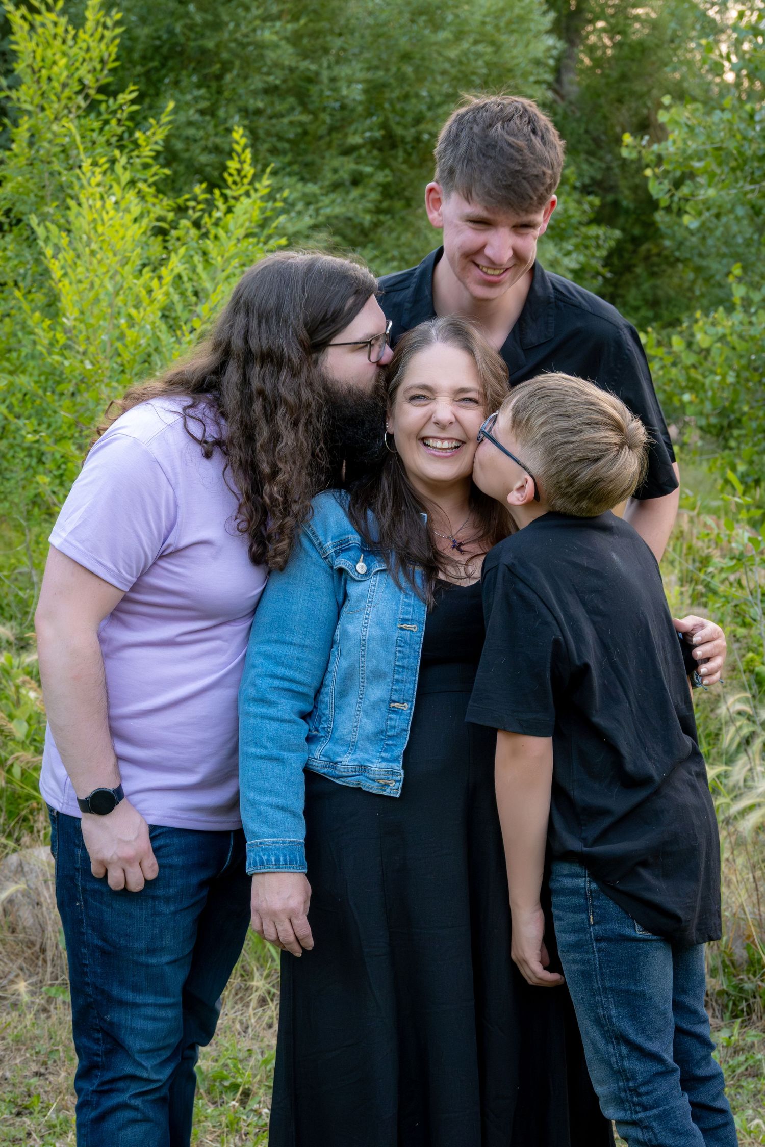 A mom and her three sons around her kissing her on the cheeks and smiling.