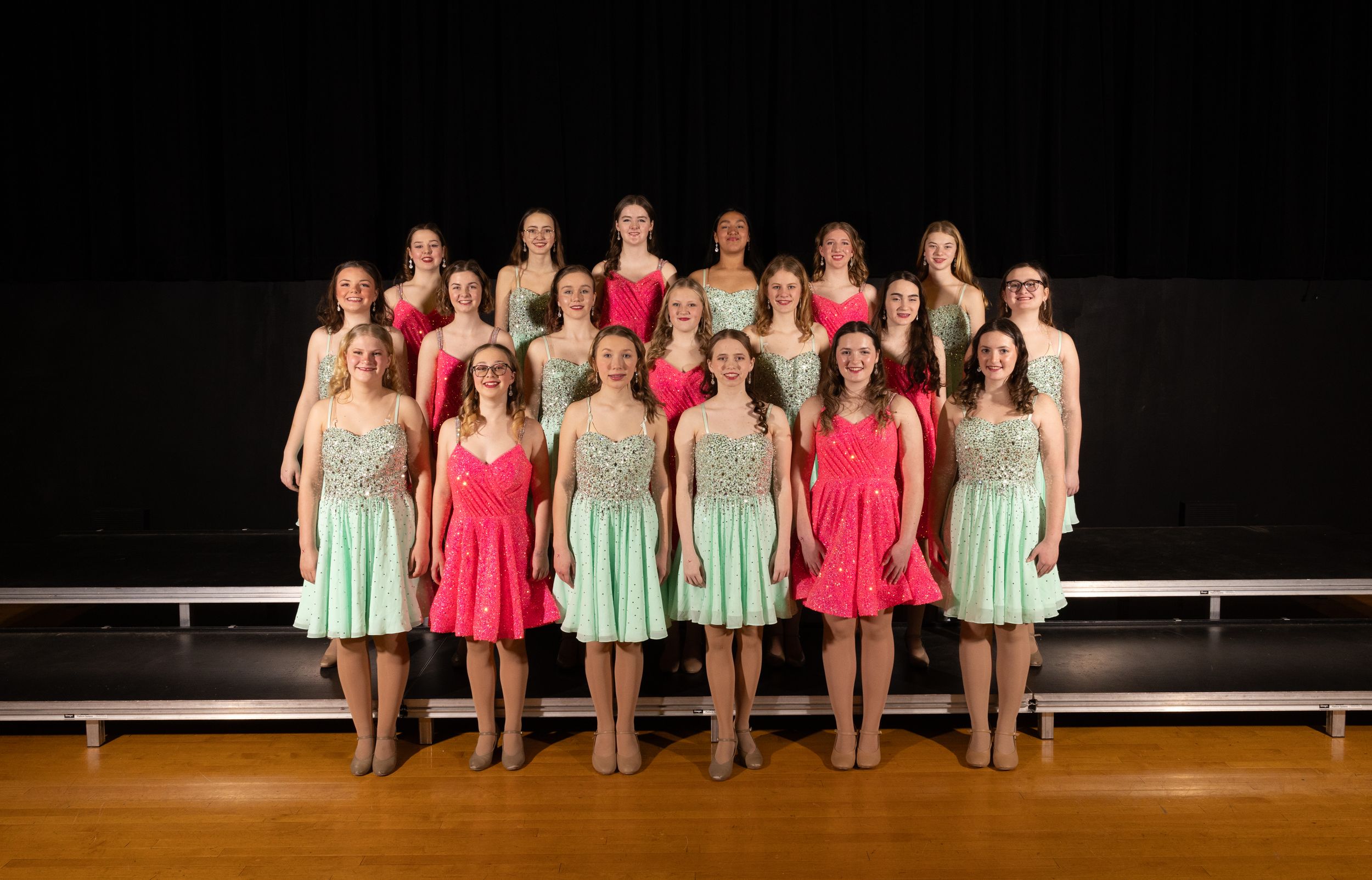 Dance ensemble wearing pink and mint colored dresses poses together on stage.