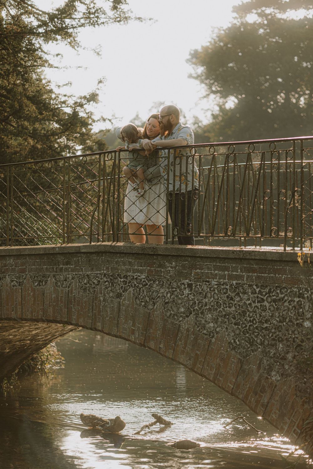 Couple shares a romantic moment on a stone bridge over water during golden hour.