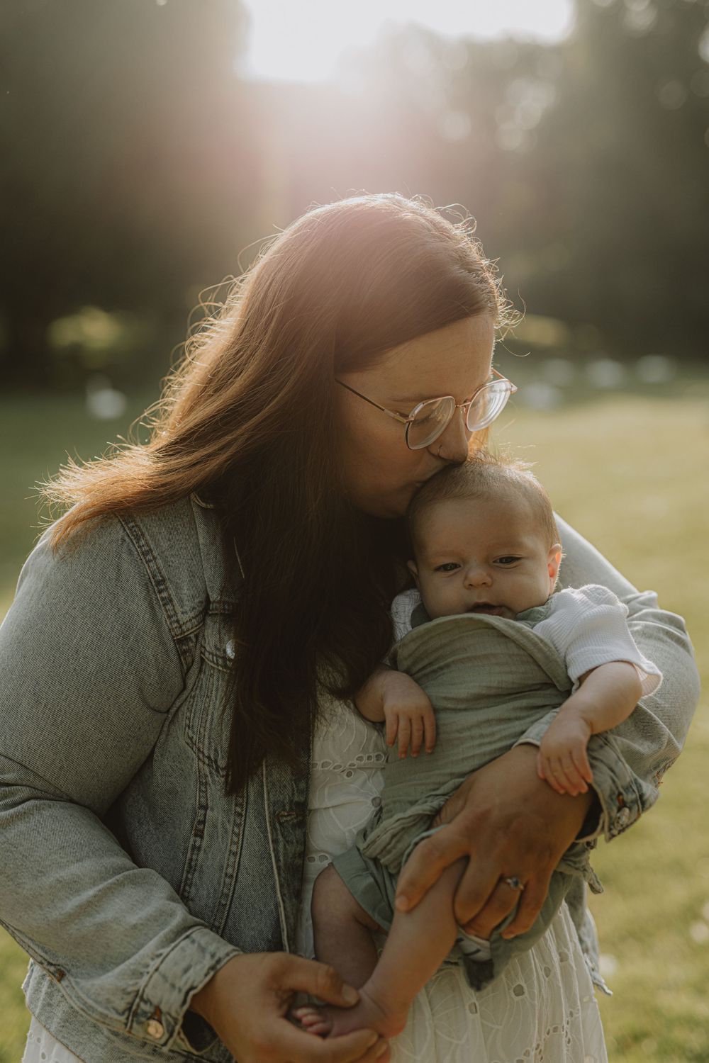 Tender moment between parent and baby in soft sunlit field wearing matching denim.