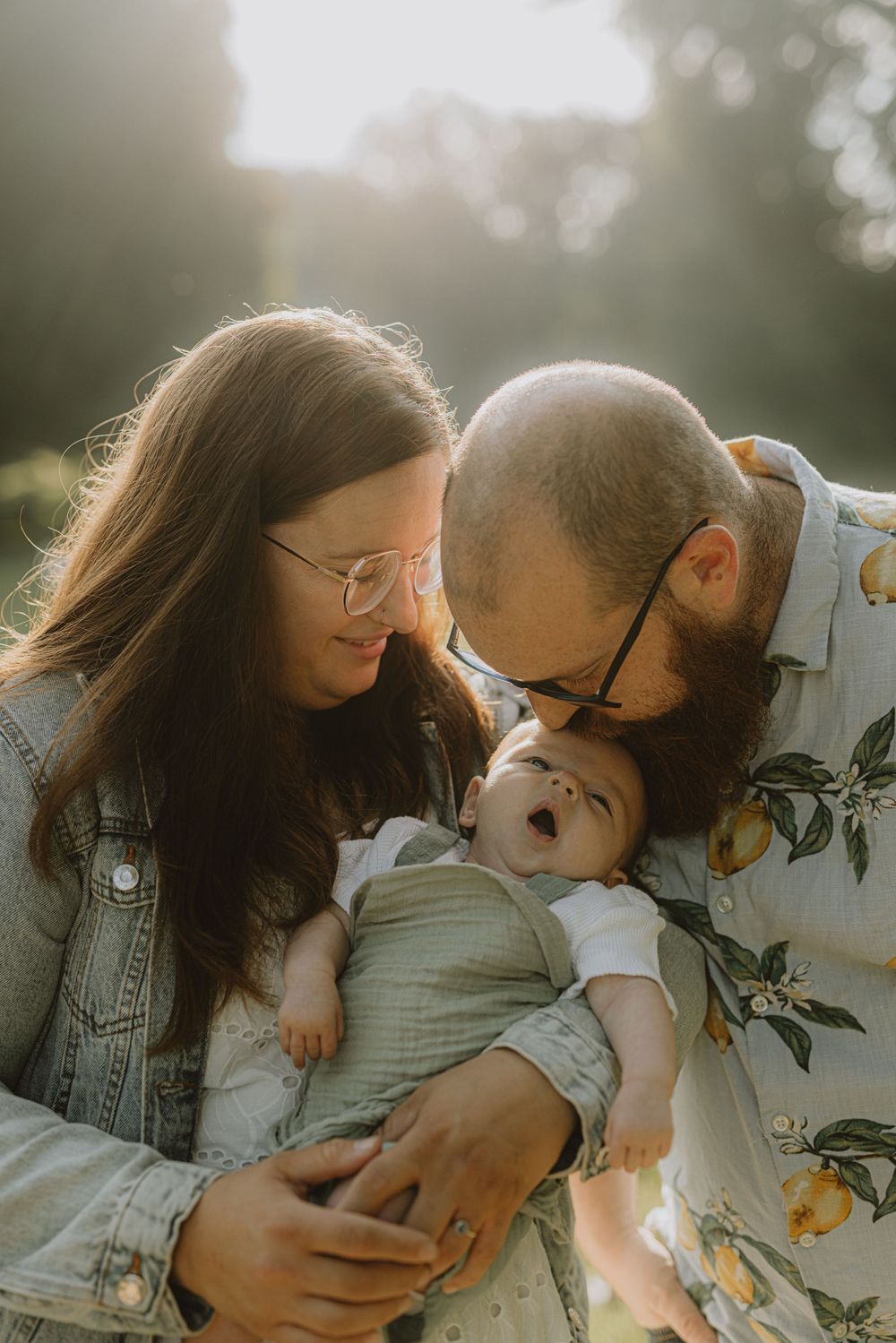 A tender family moment captured in golden sunlight as parents share a loving interaction with their baby.