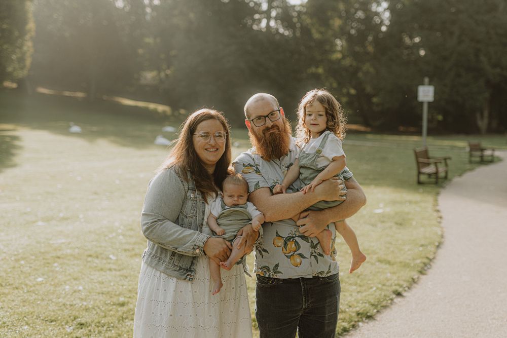 Family of four poses together on a sunny path in a park with natural backlighting.