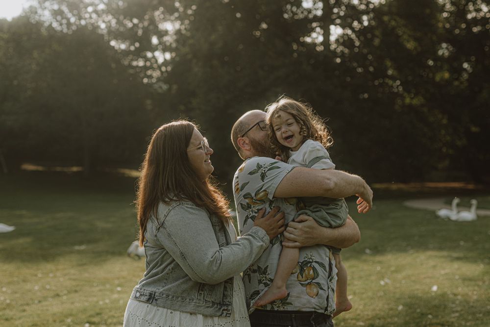 Candid family portrait in a park with sunset lighting and swans in background.