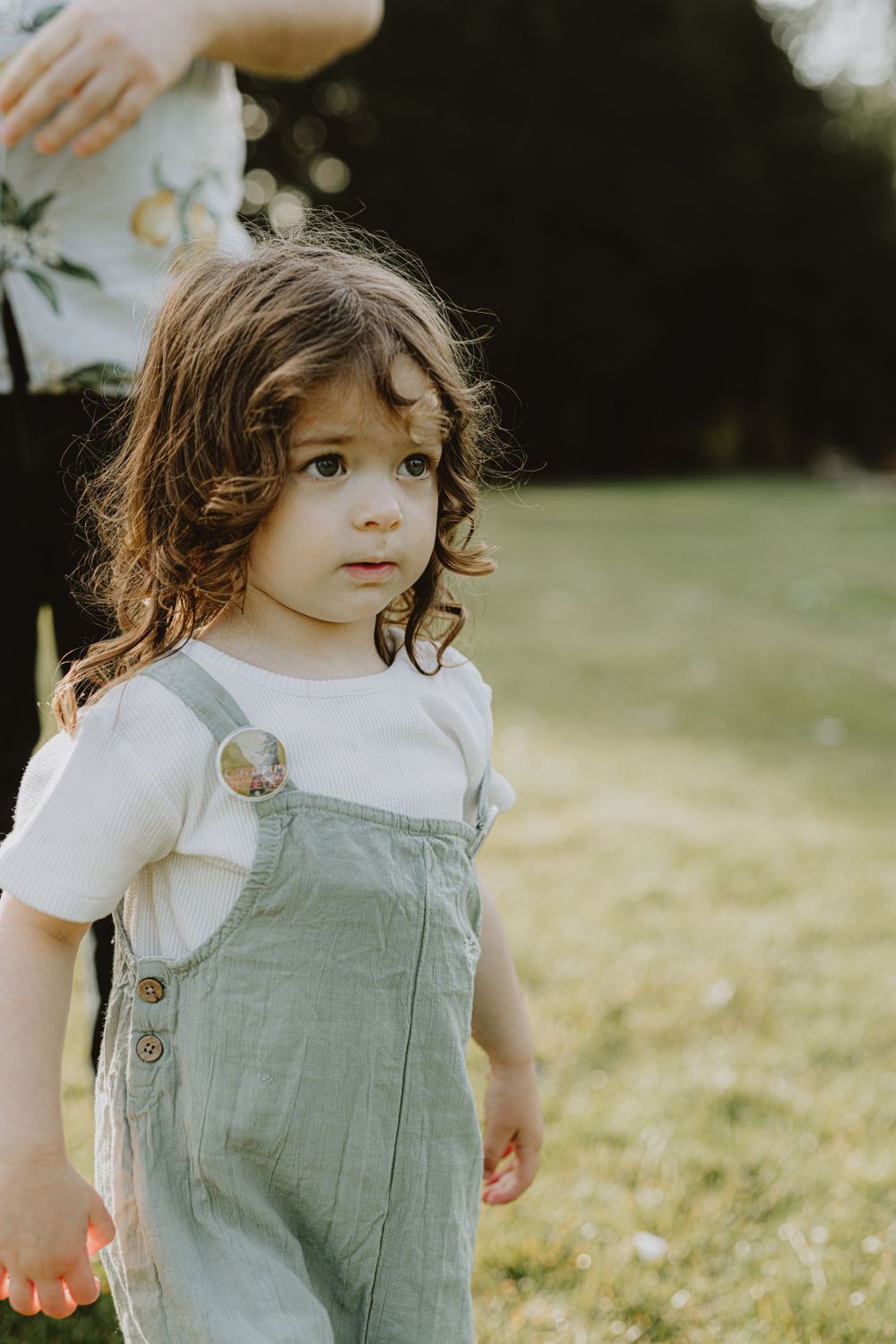 Young child in light blue overalls standing in a sunlit field.