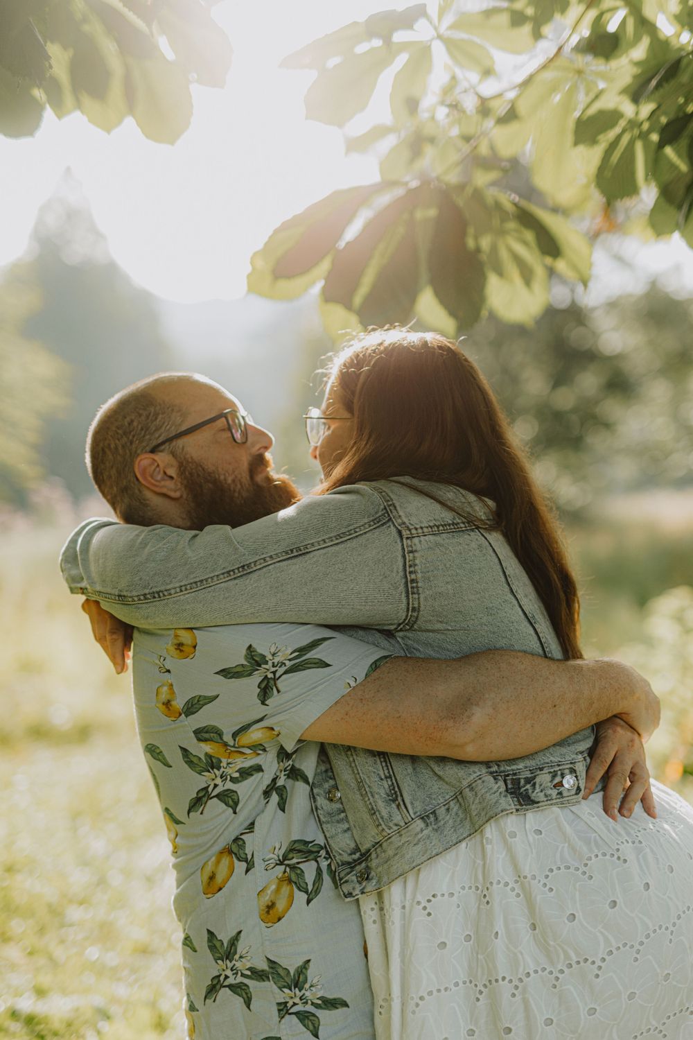 A couple embraces in golden sunlight under tree branches with yellow flowers.