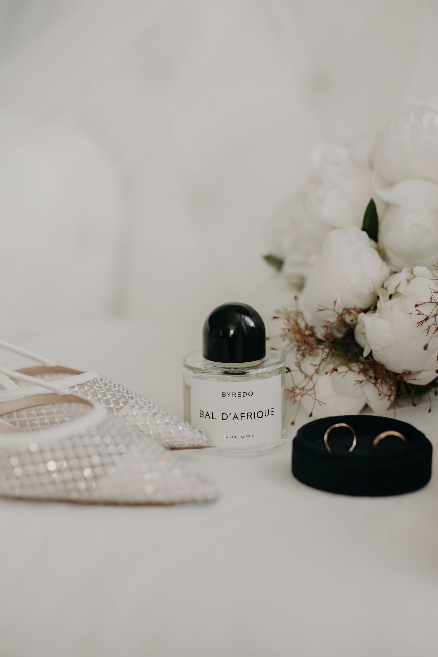 Elegant perfume bottles and white flowers arranged on a light surface with a delicate lace pattern.