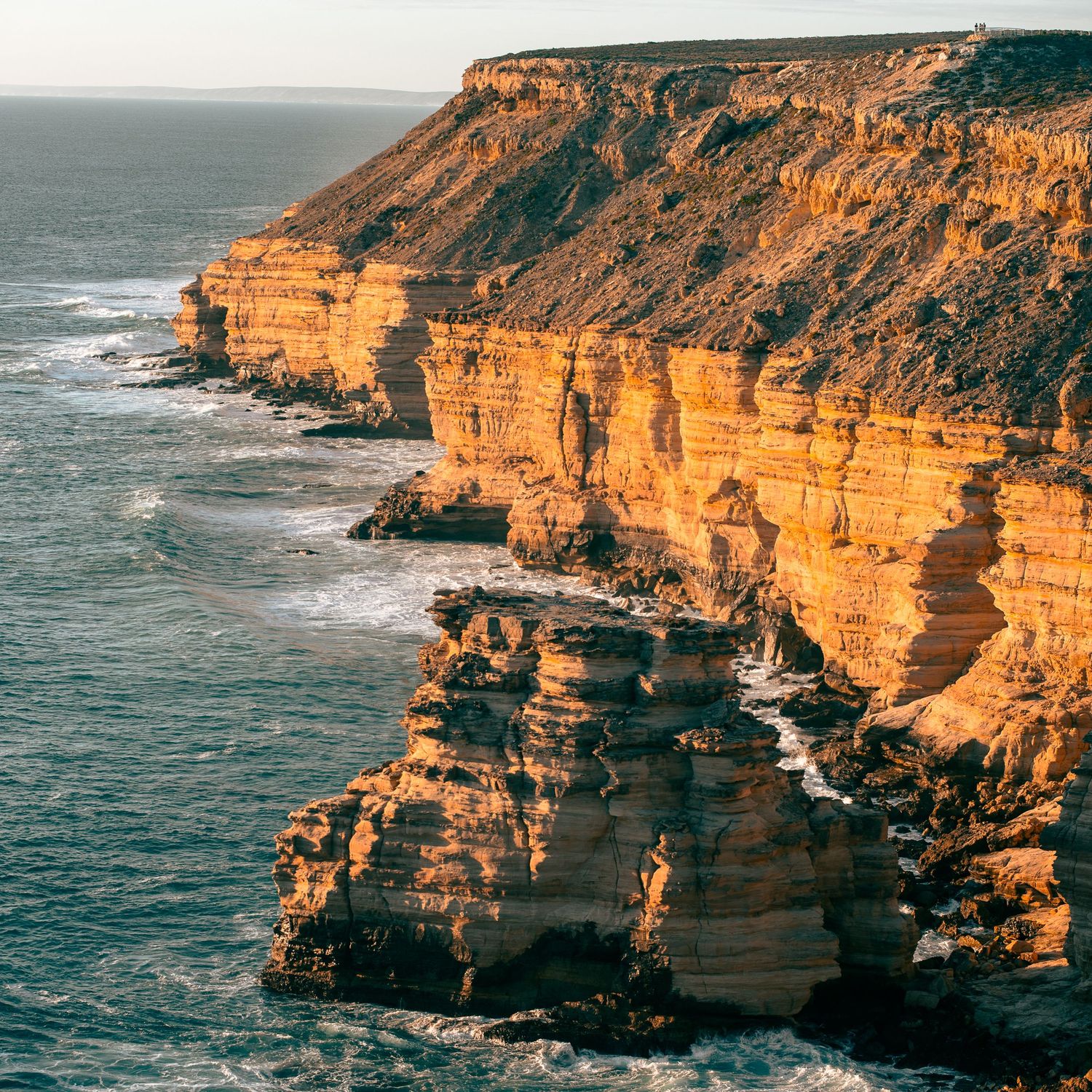 Dramatic coastal cliffs and rock formations along ocean shore during golden hour.