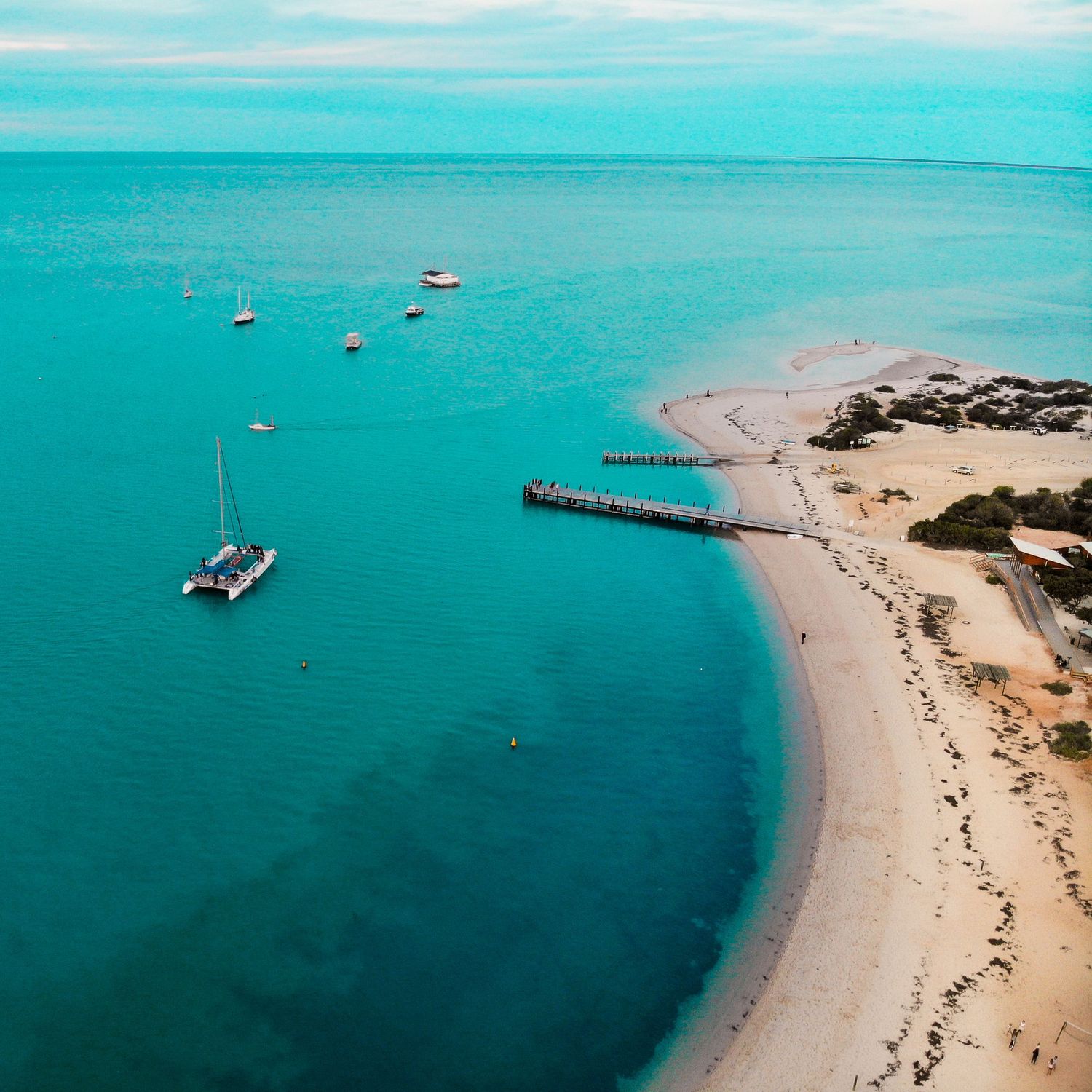 Aerial view of turquoise waters with boats anchored near sandy beach and pier.