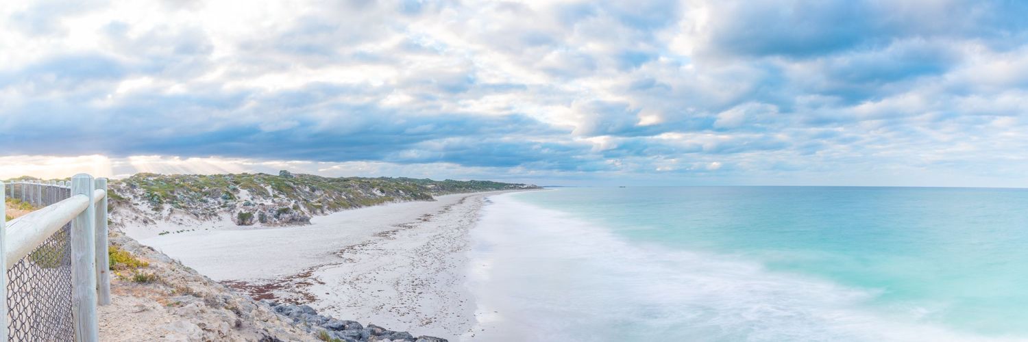 A pristine white sandy beach stretches along turquoise waters under a cloudy sky.