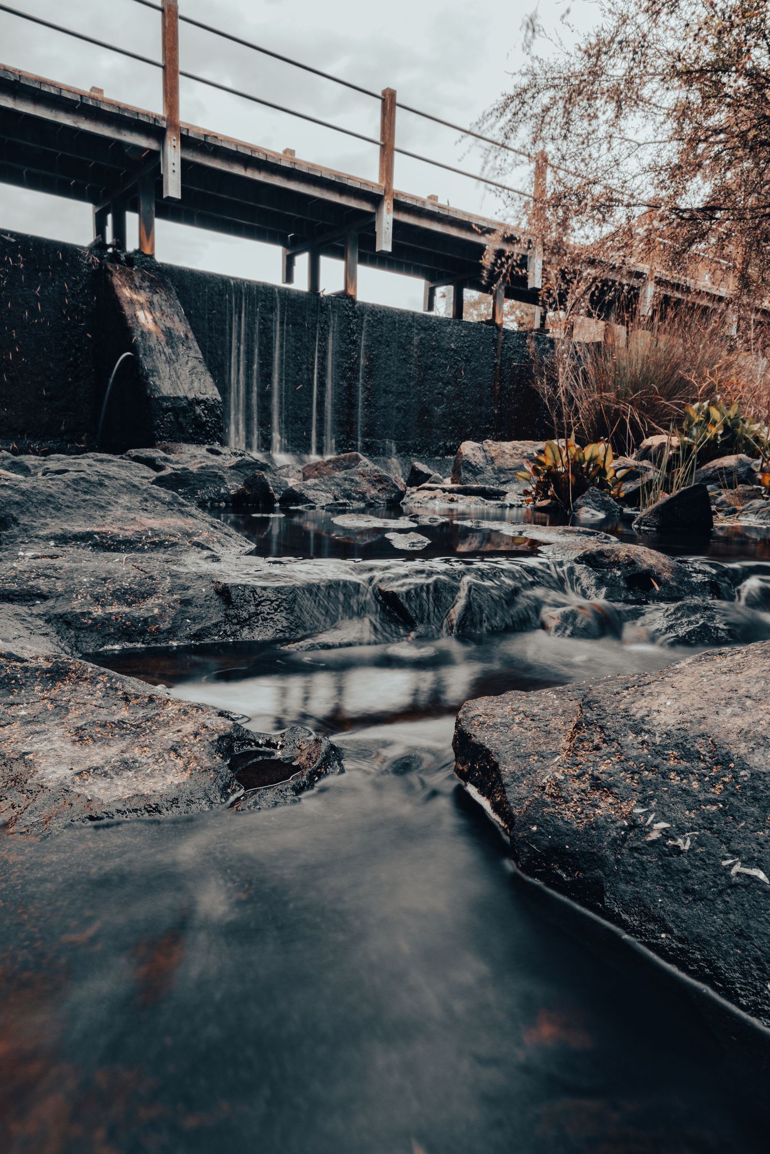 Long exposure of a rocky stream flowing under a bridge with dark moody tones.