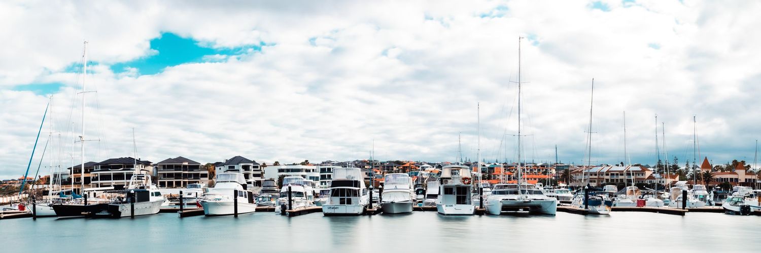 A panoramic view of a marina filled with boats and yachts under scattered white clouds.