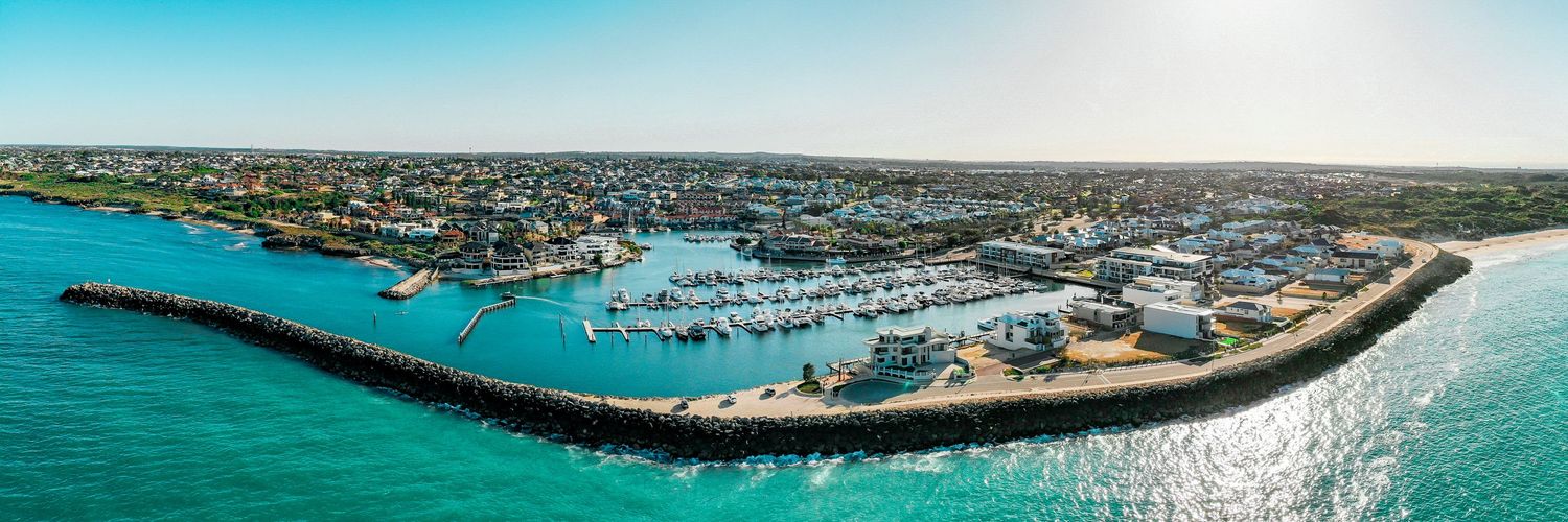Aerial panorama of a coastal marina with turquoise waters and boats docked along the breakwater.