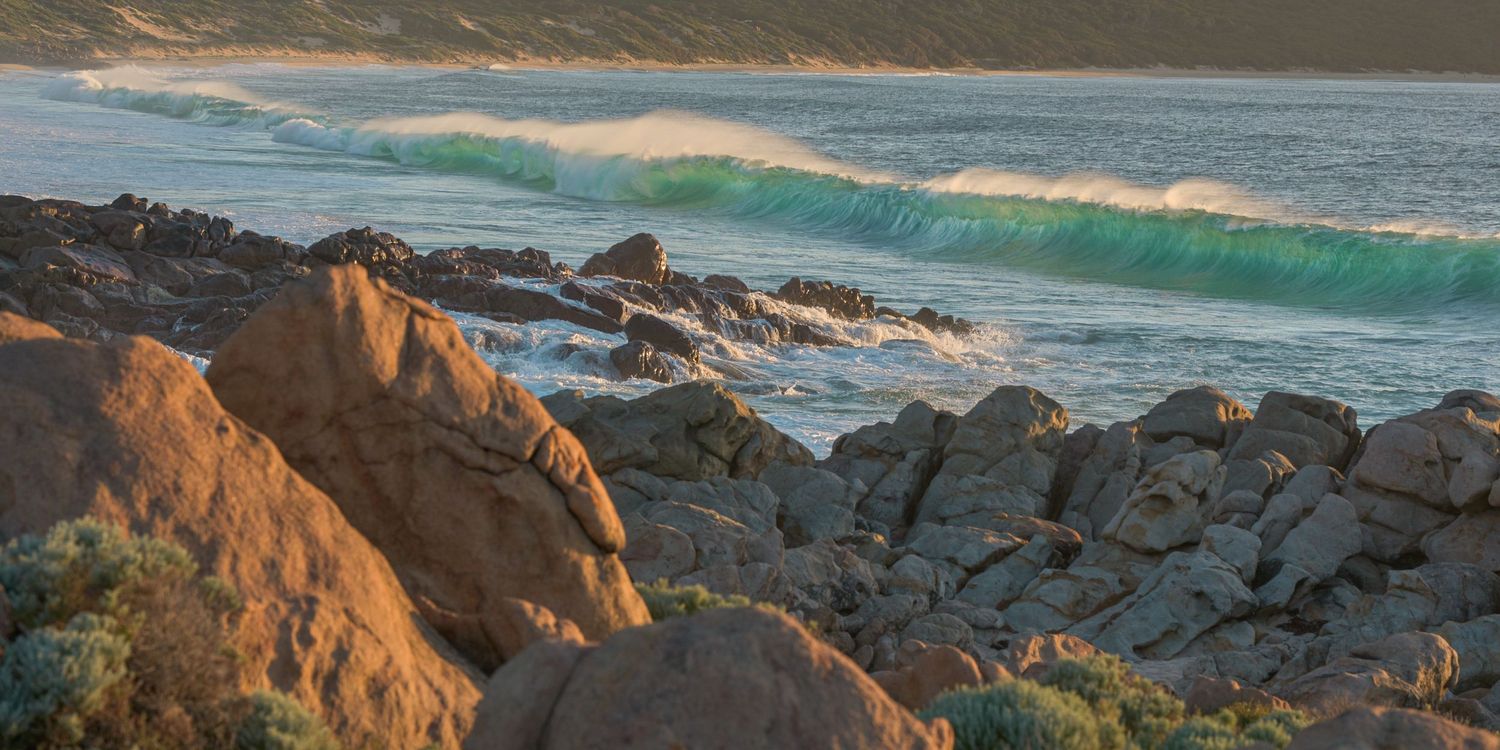 Ocean waves crash against golden rocky cliffs during sunset along a dramatic coastline.