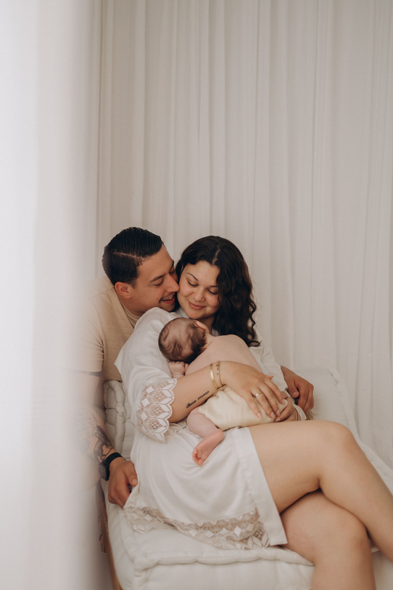 Intimate maternity photo of couple relaxing together against white backdrop.