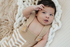 Baby in beige outfit lying on cream textured blanket during newborn photoshoot.