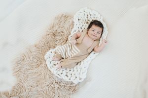 Newborn baby resting on soft white knitted blanket with neutral tones.