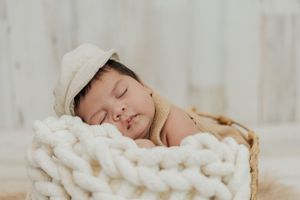 Peaceful sleeping baby wrapped in chunky knit blanket during newborn session.