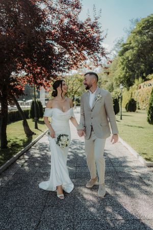 Newlyweds share a romantic moment walking together on a gravel path under red autumn trees.