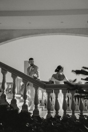 Black and white photo of a wedding couple silhouetted against white balustrades on a sunny day.