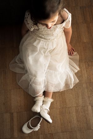 Close-up views of white dress and shoes on wooden floor showing delicate details of formal children's attire.