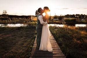 Silhouetted couple embraces on wooden boardwalk at sunset with golden light streaming through marsh landscape.