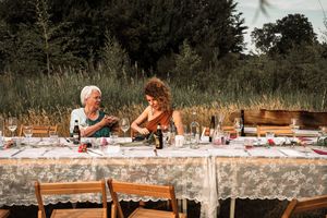 A rustic outdoor dinner party setup with a long table covered in lace tablecloth and wooden chairs in a garden setting.