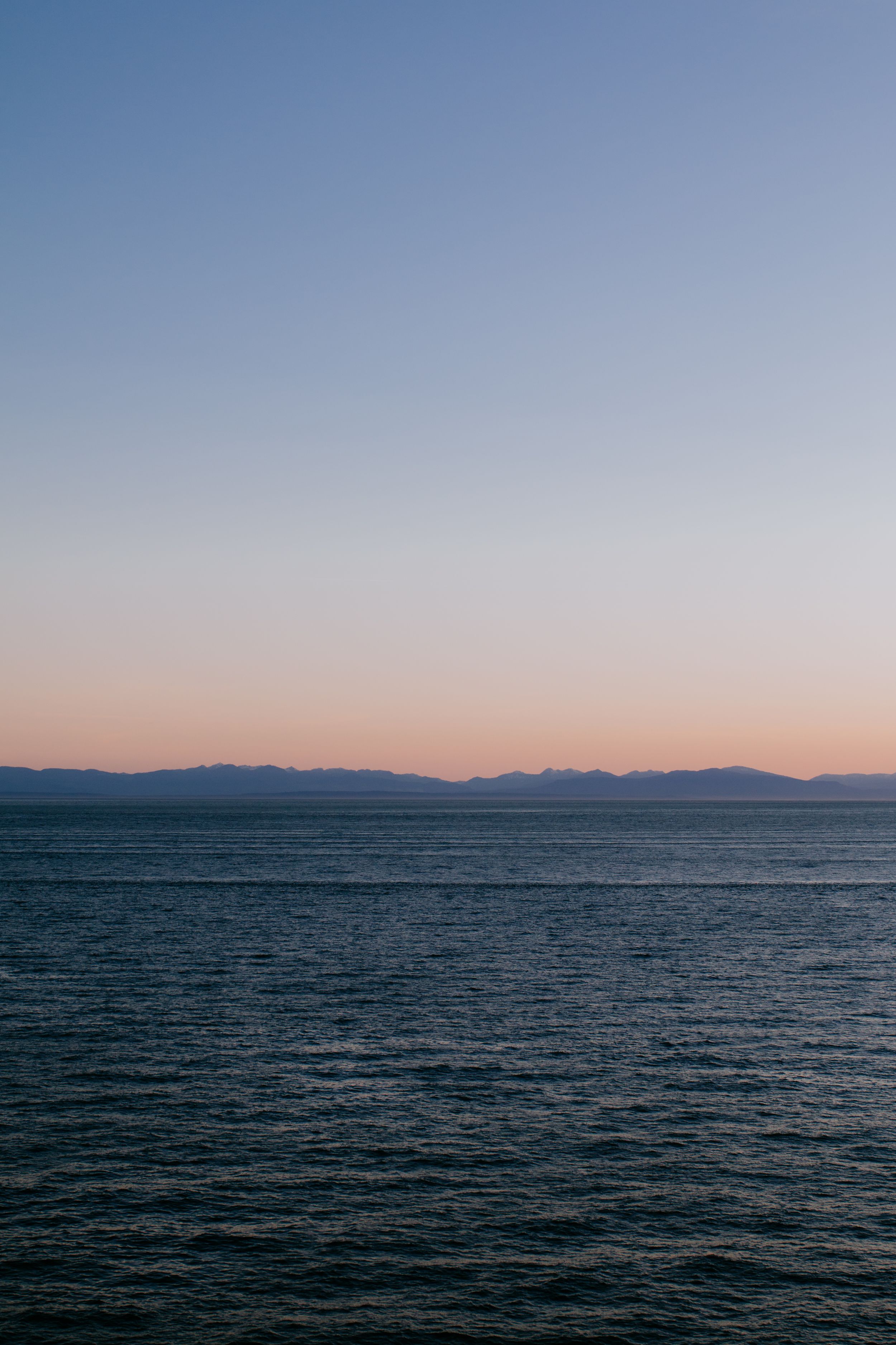 Minimalist seascape with mountains silhouetted against gradient sky at dusk.