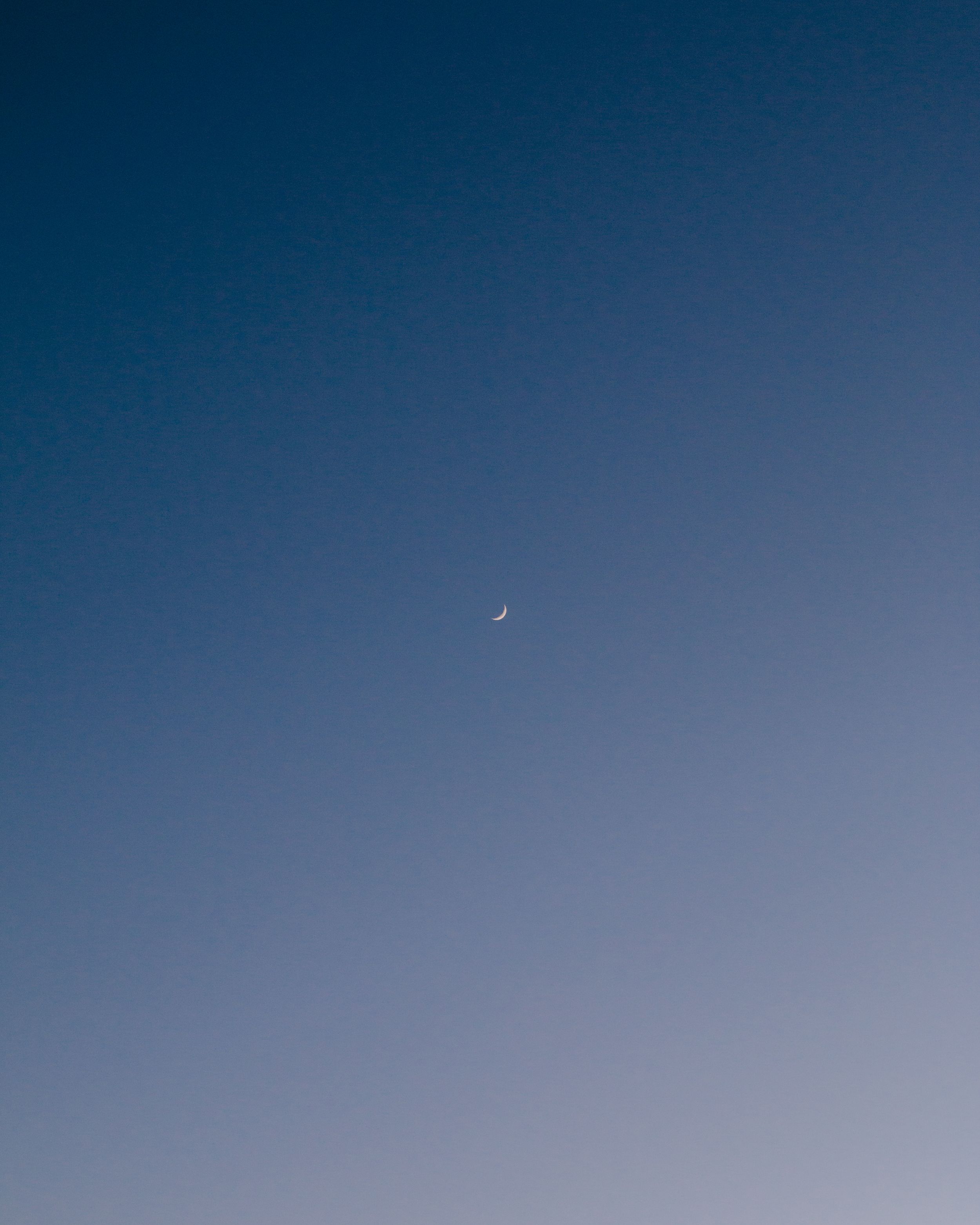 Crescent moon in clear deep blue gradient sky.