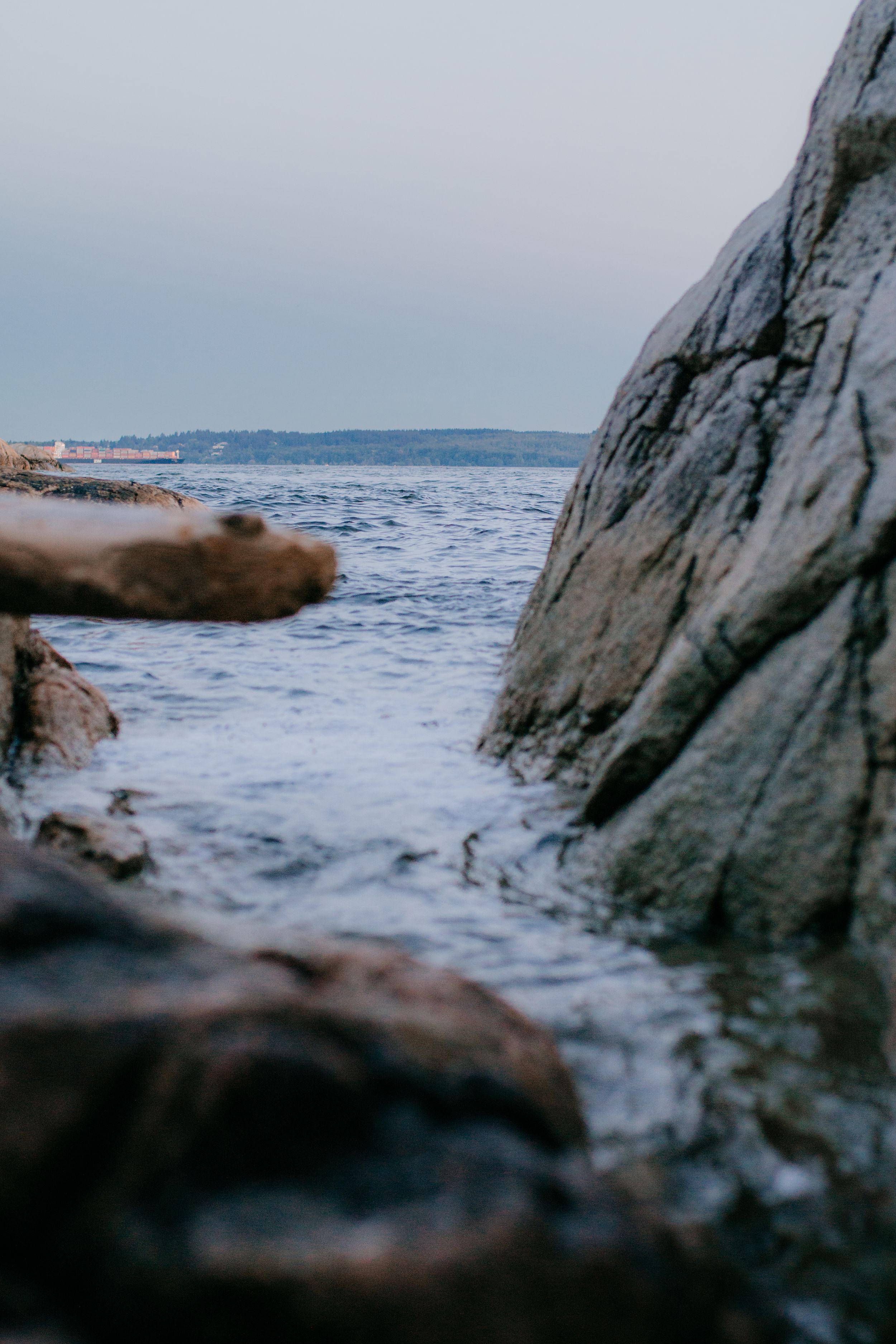 Close-up view of rocky coastline with waves crashing against dark stones at the ocean's edge.