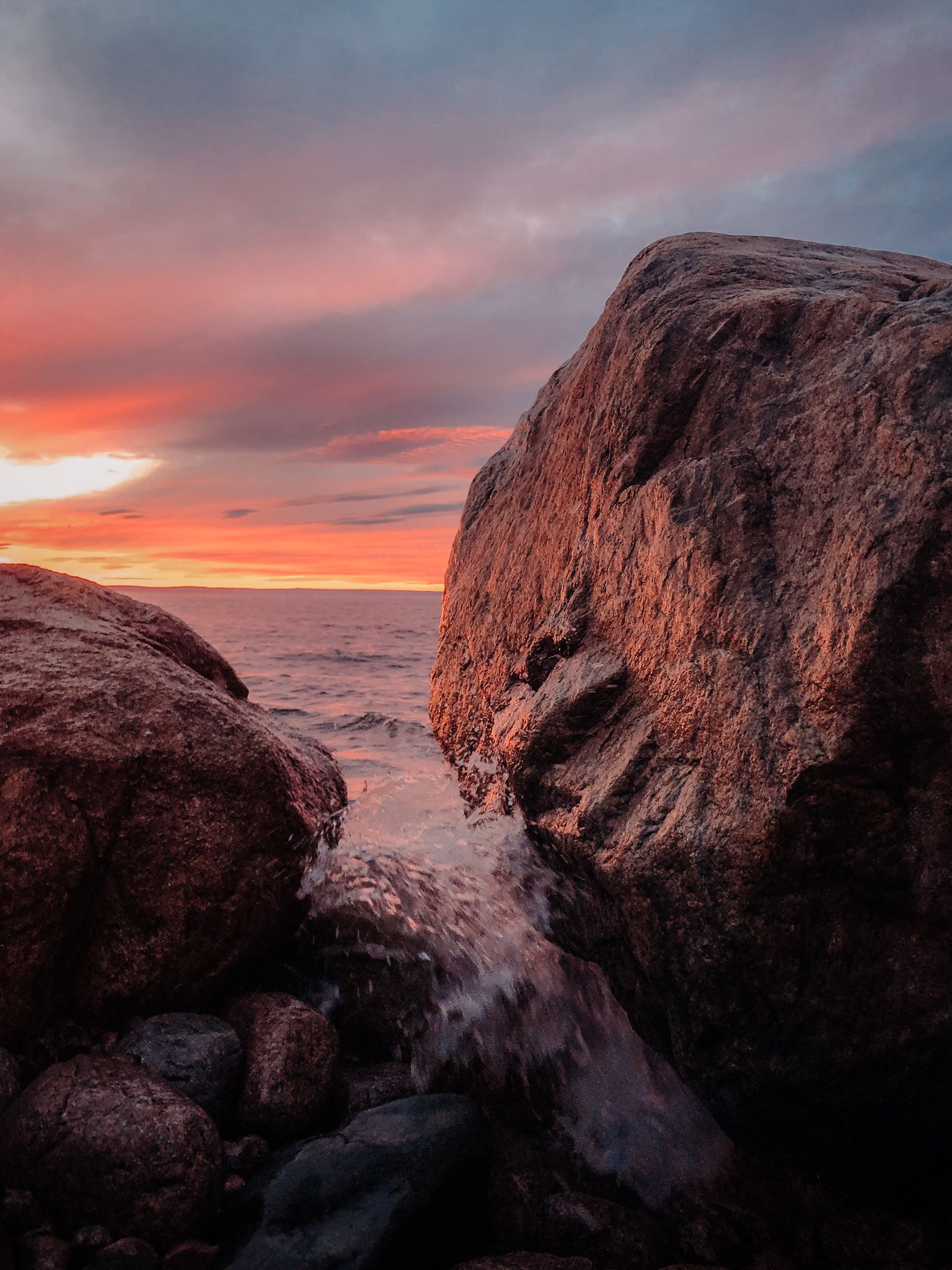 Sunset over rocky coastal formations with dramatic orange sky and crashing waves.