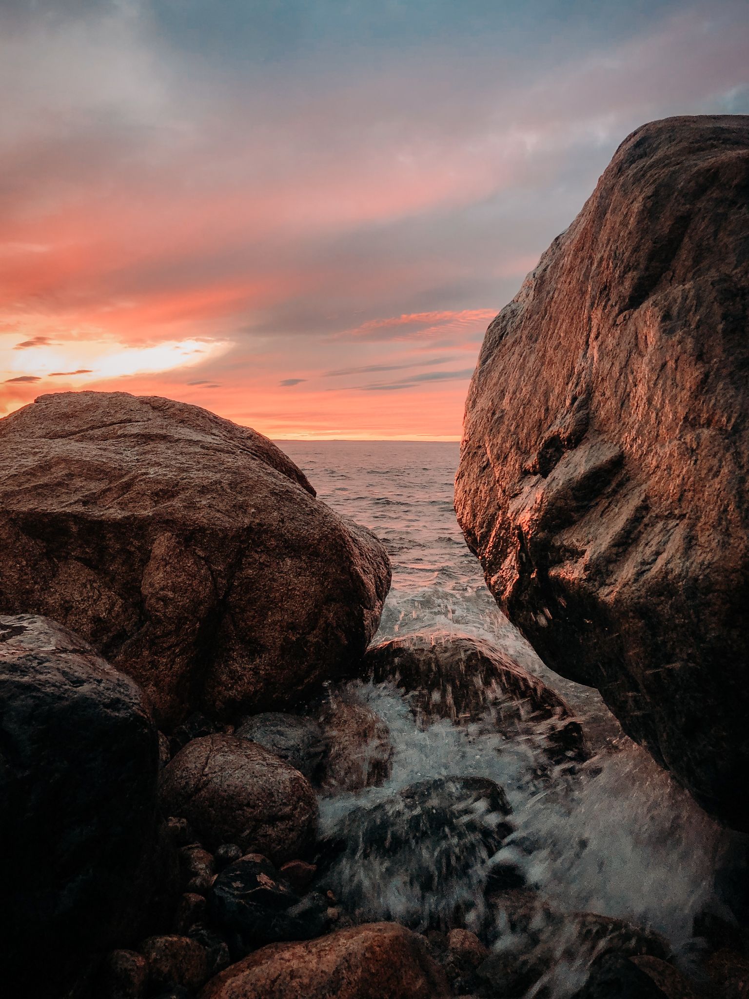 Ocean waves crash between large coastal rocks during a vibrant sunset.