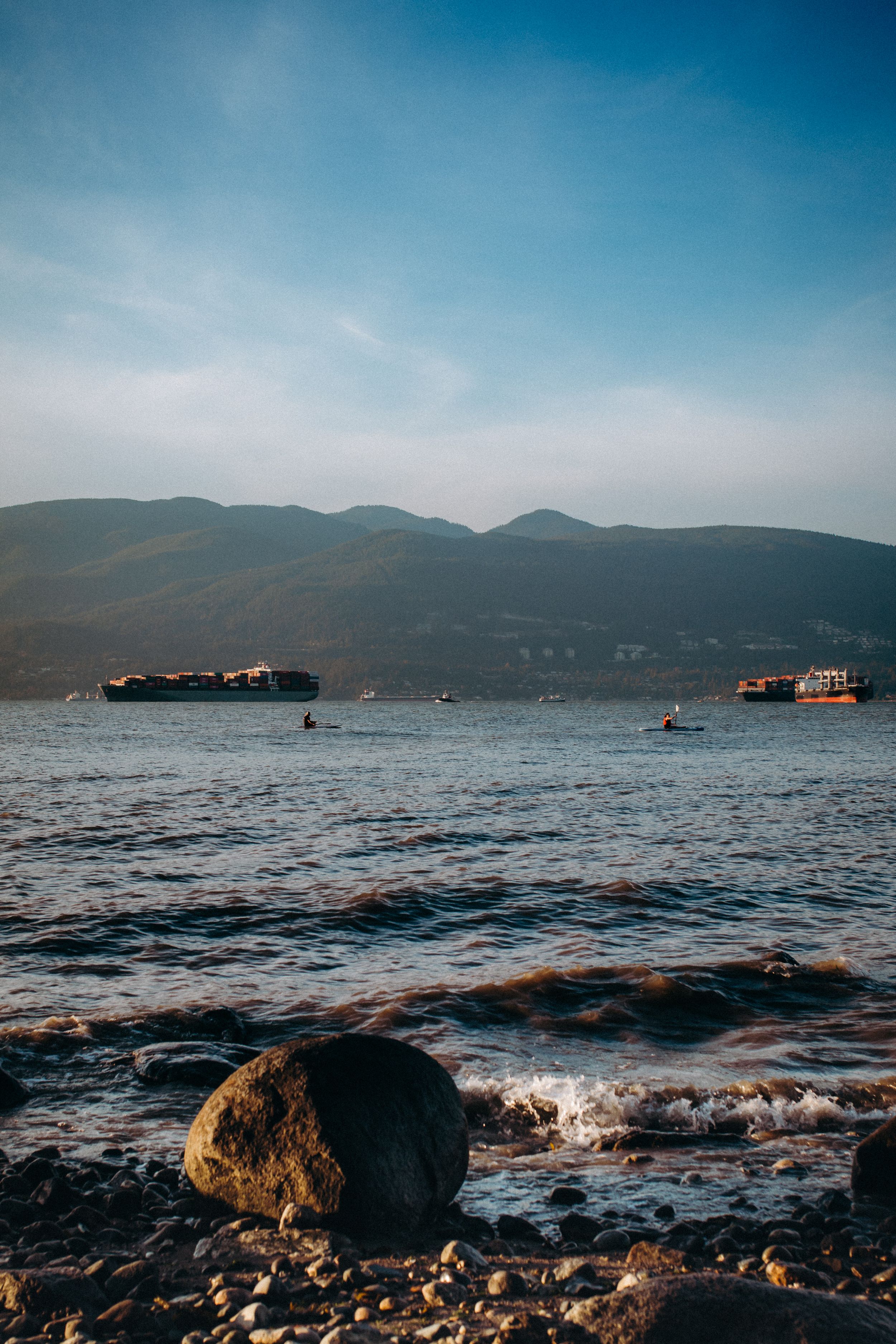Rocky shoreline with mountains and cargo ships visible across the calm waters.