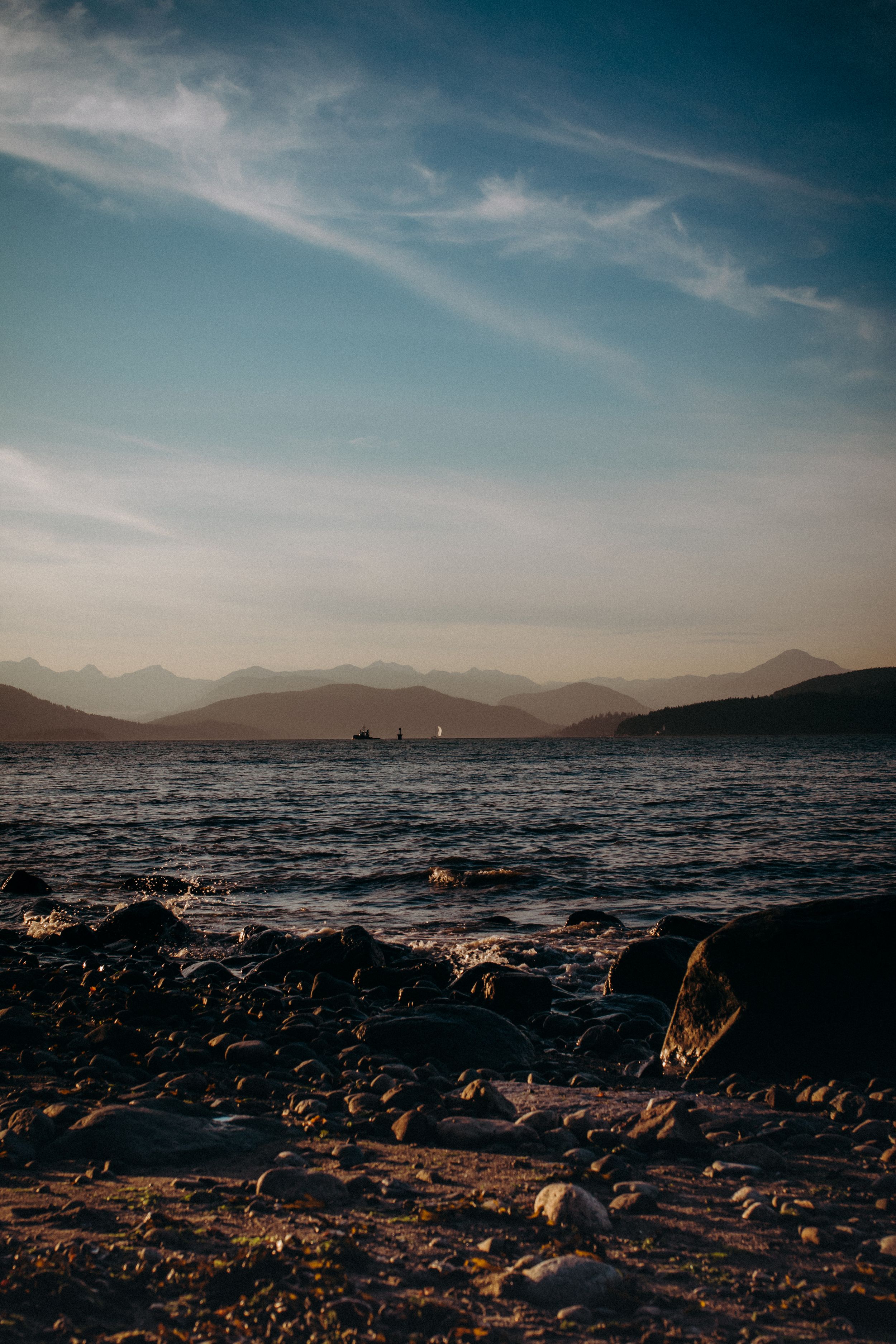 Rocky beach with distant mountains and calm waters under a clear sky at golden hour.