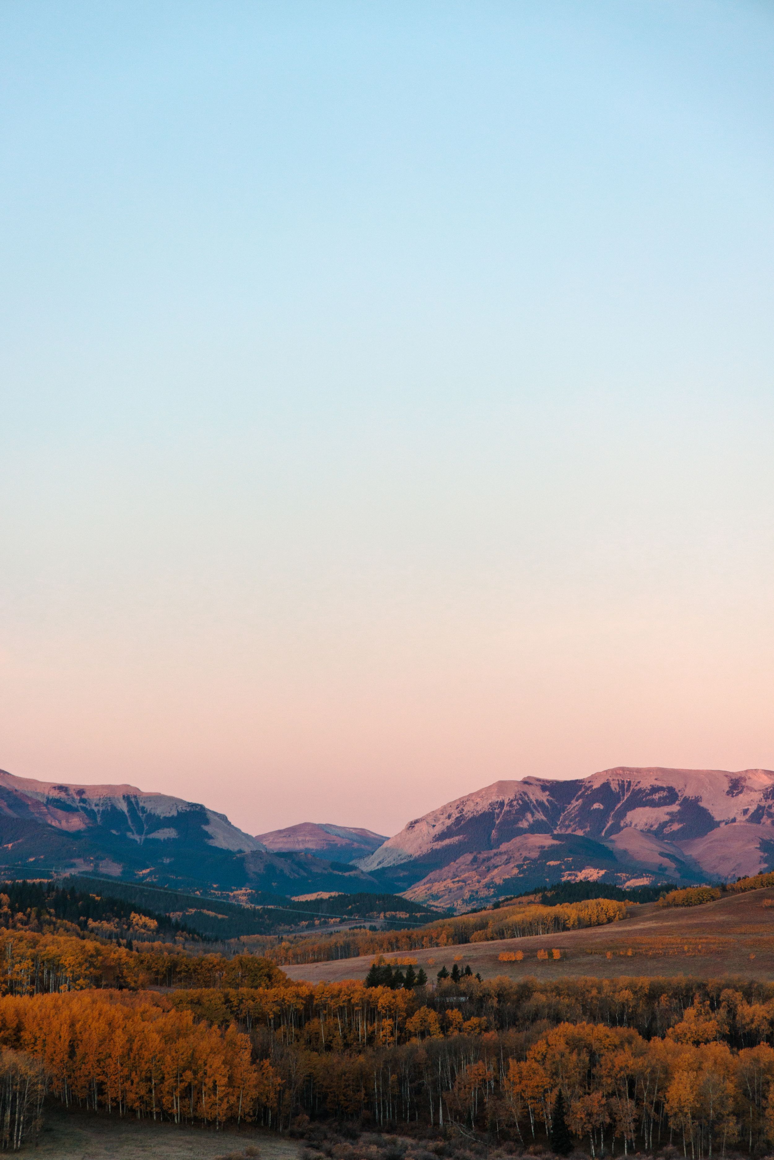 Mountain landscape at dusk with fall foliage and pastel gradient sky.