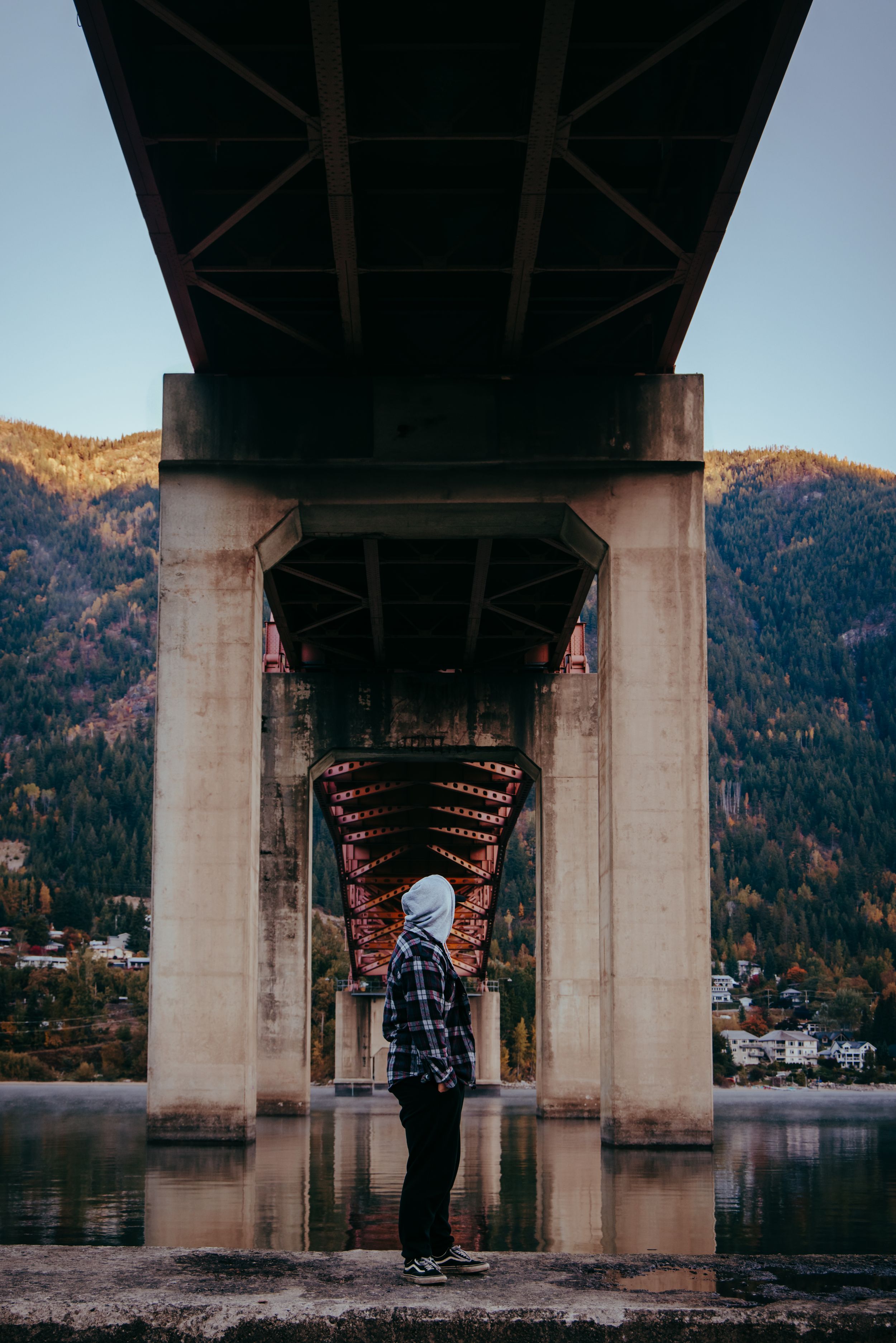 Silhouette under a bridge support with mountains and water in background.
