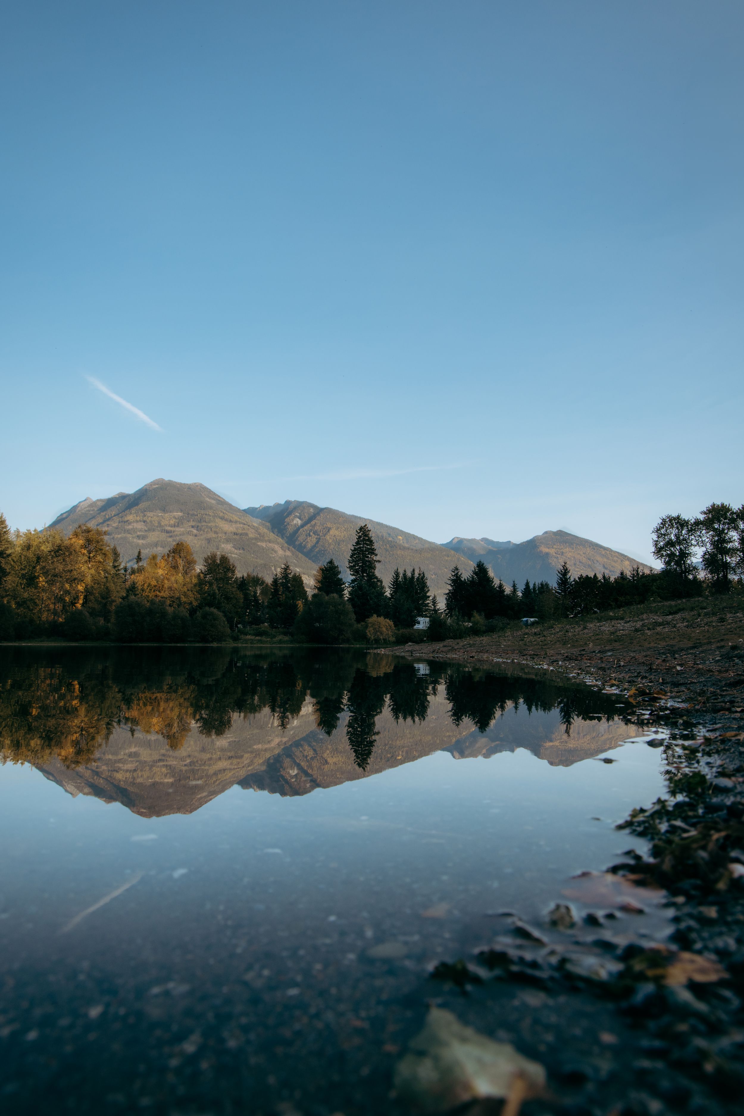 Mountain reflection in still lake water with autumn trees along rocky shore.
