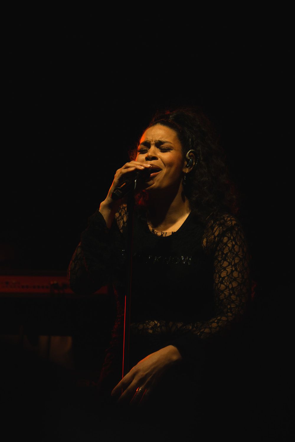 Female vocalist singing passionately into a microphone under warm stage lighting in a black lace top.