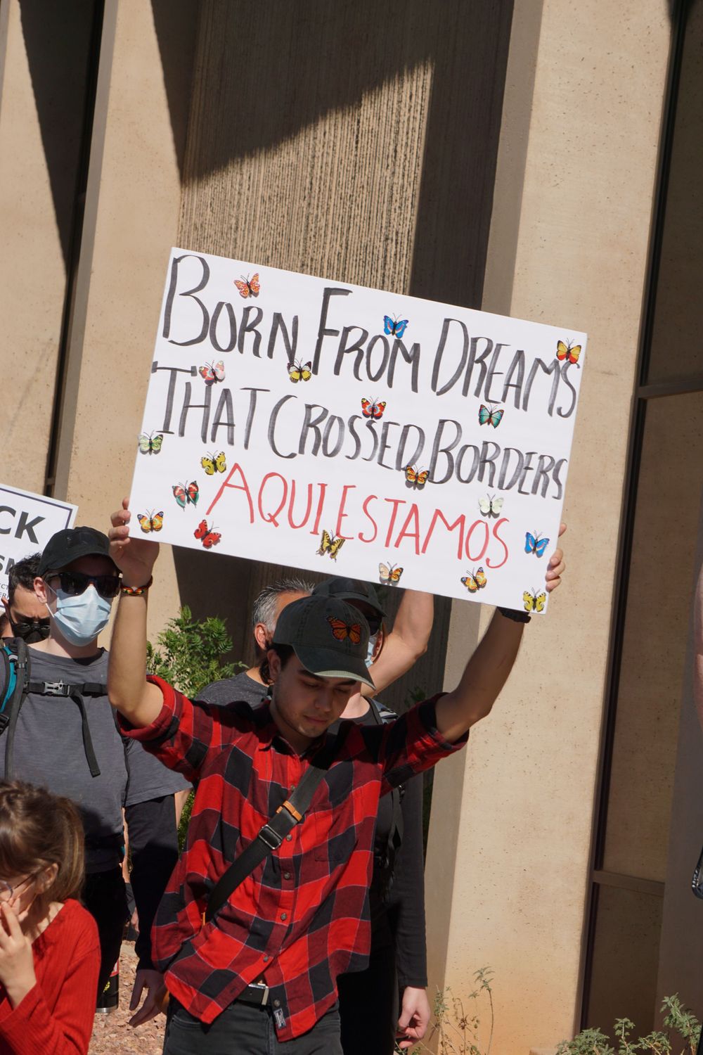 Protest sign reading 'Born from dreams that crossed borders' with decorative butterflies.