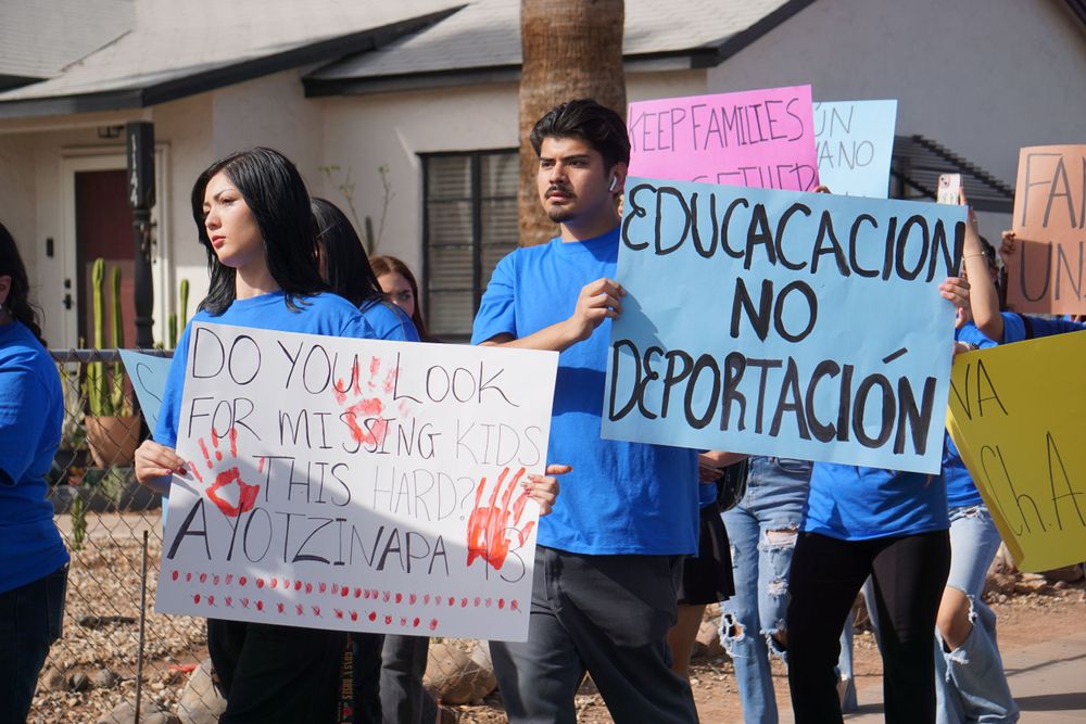 Students holding protest signs with Spanish text at outdoor demonstration.