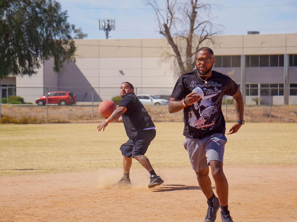 Two players run on a dusty field during a casual game of flag football on a sunny afternoon.