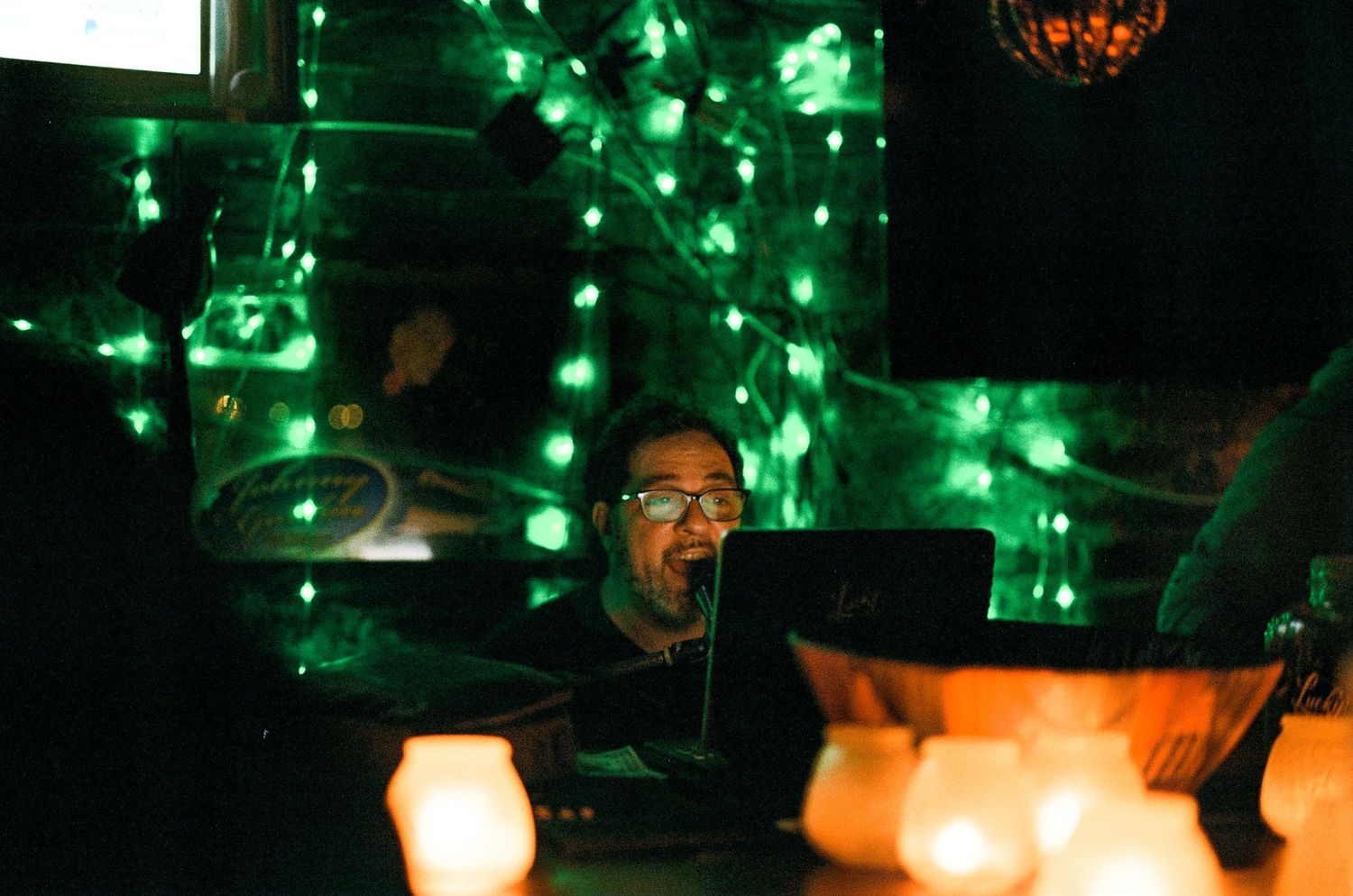 Green string lights create an ambient glow in a dark bar or restaurant setting.
