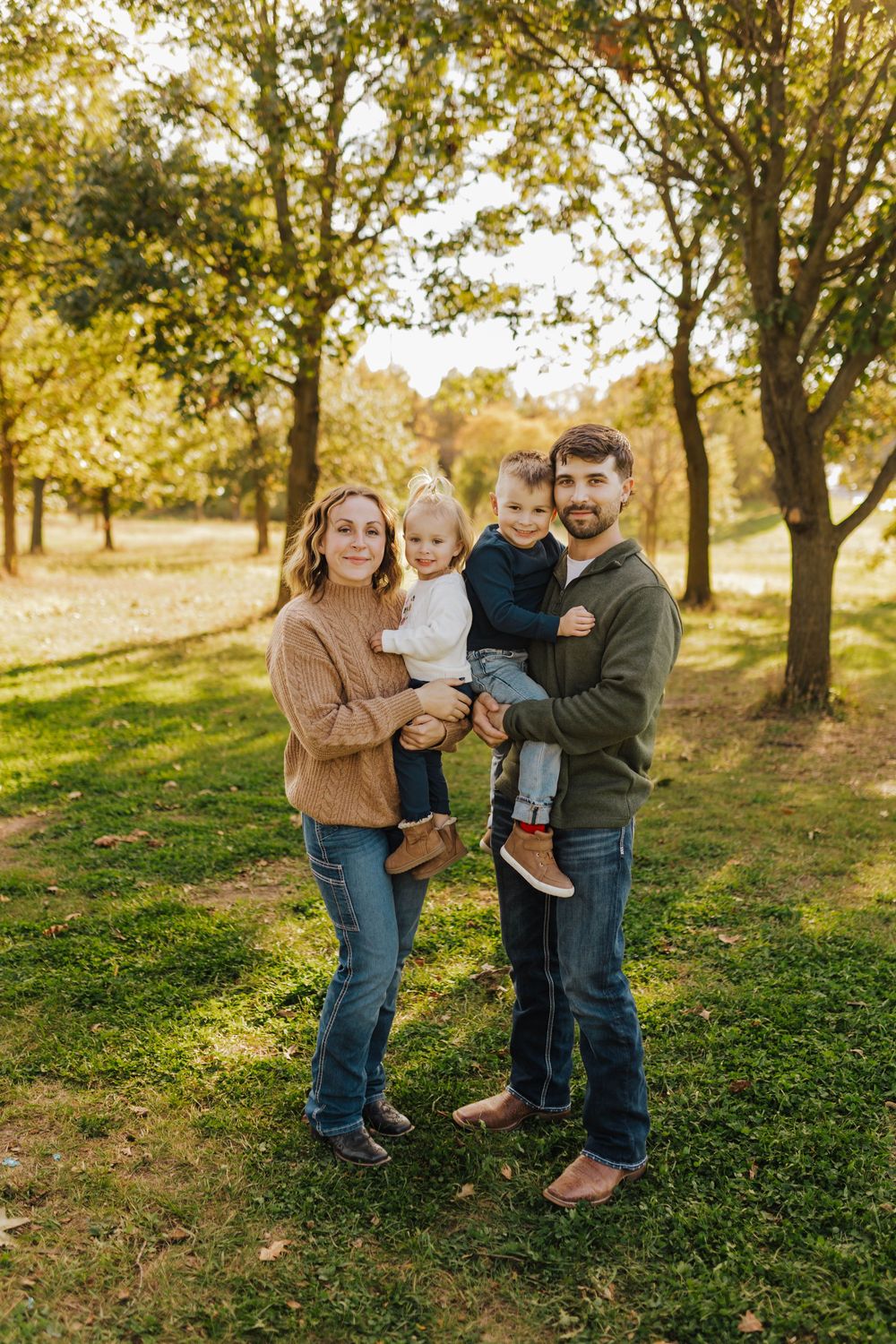 A family enjoys a warm autumn day together in a sunlit orchard with golden leaves and green grass.