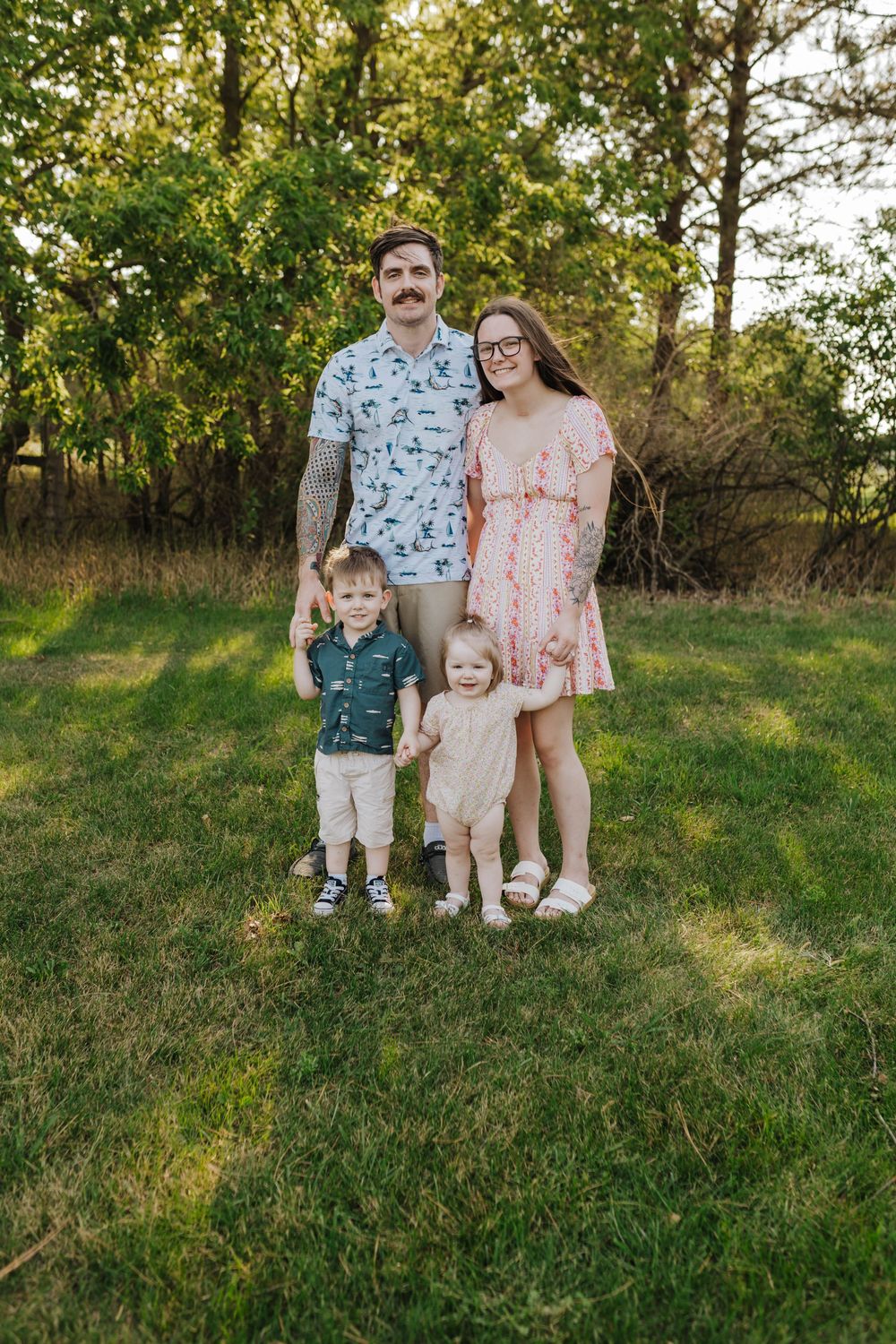 A family stands together on a grassy hillside during golden hour wearing coordinating floral and patterned outfits.