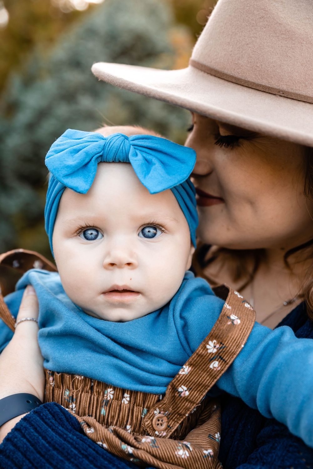 Close-up of a baby wearing a blue headband and brown overalls.