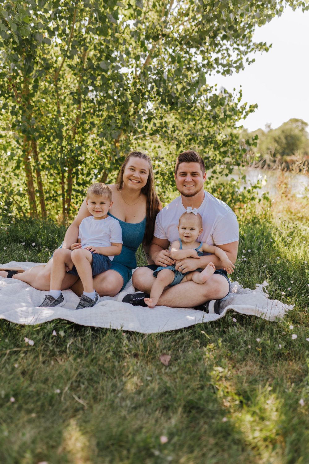A family picnic scene by a lake with green trees in the background.