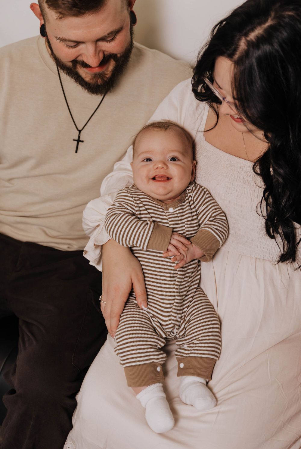 A family in neutral-toned clothing shares tender moments with their smiling baby in a series of candid lifestyle photos.